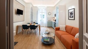 Una sala de estar moderna con un sofá, un comedor con sillas y una mesa, una zona de cocina y un televisor montado en la pared.