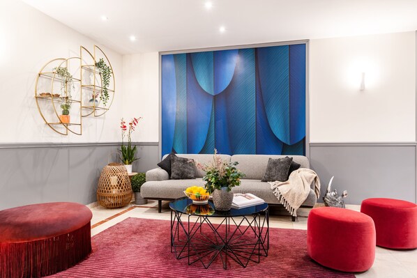 A modern living room with a grey sofa, red ottomans, a coffee table with a vase of flowers, and a large abstract painting on the wall.