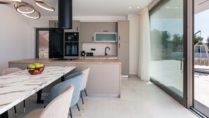 Una cocina moderna con una isla central, un comedor con sillas y un amplio ventanal corredero al exterior.