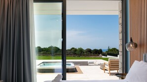 Habitación de hotel moderna con una cama grande, vista a un jacuzzi y un área de estar al aire libre.
