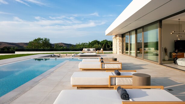 Un área de piscina moderna al aire libre con sillones de descanso y una vista despejada de las montañas.