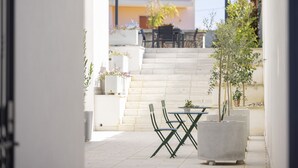 An outdoor patio with a table and chairs, potted plants, and a staircase leading to a covered area. - Dimora Lauro (Gagliano del Capo)