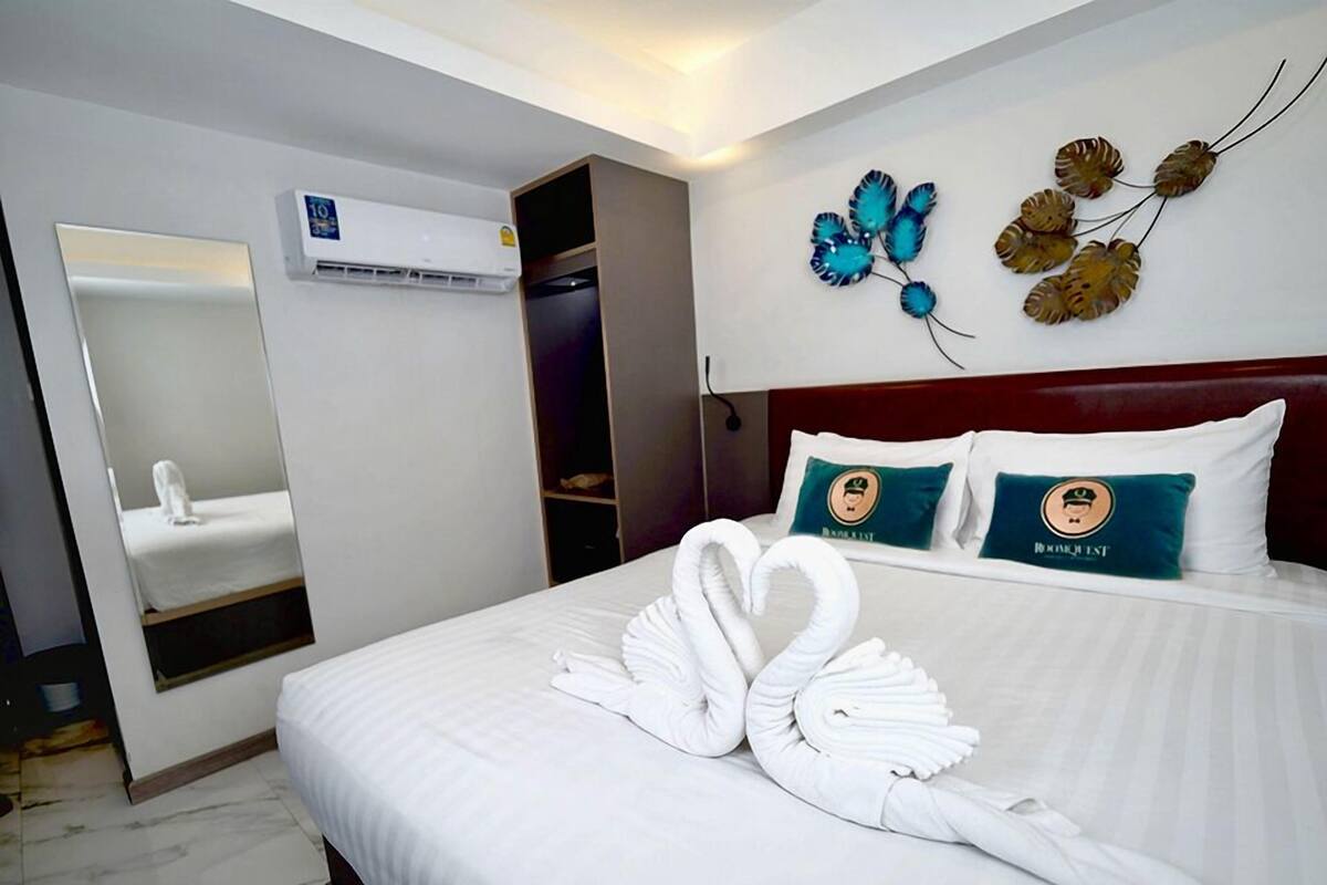 Une chambre d’hôtel avec un lit bien fait, une salle de bain avec un miroir et un lavabo, et un élément décoratif sur le mur.