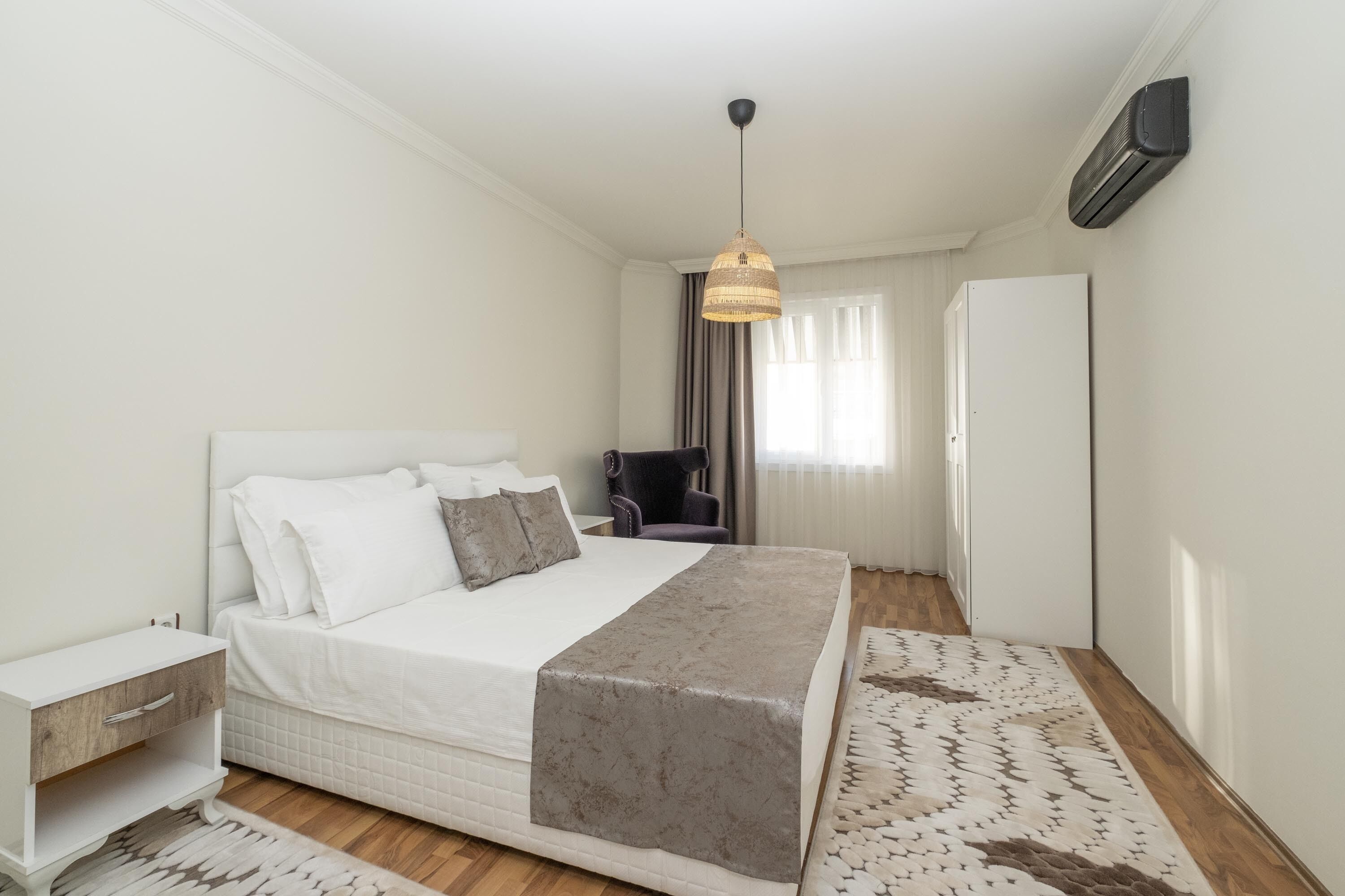 A bedroom with a bed, bedside table, chair, and a hanging light fixture.