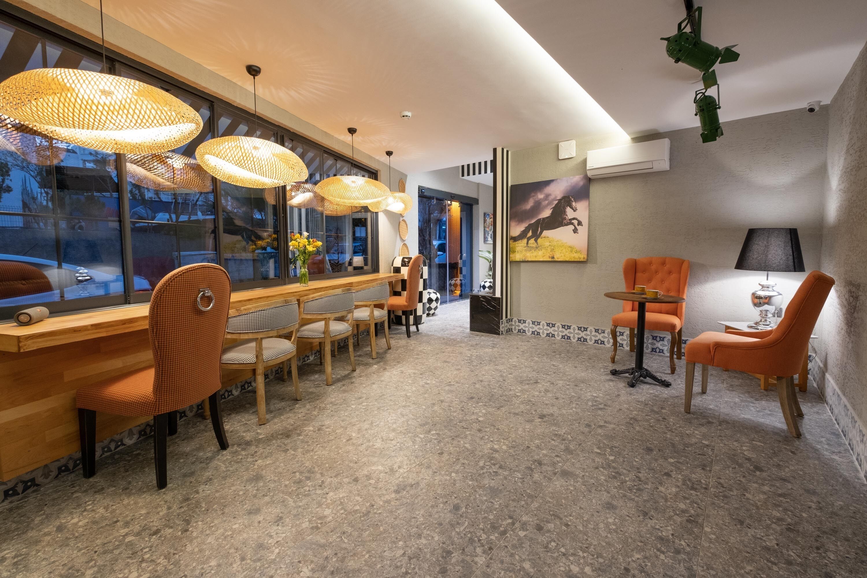 A modern hotel lobby with a long reception desk, wicker hanging lamps, and a mix of seating options including chairs and sofas.