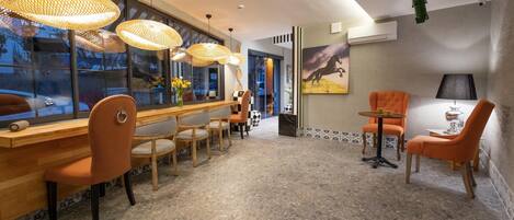 A modern hotel lobby with a long reception desk, wicker hanging lamps, and a mix of seating options including chairs and sofas.