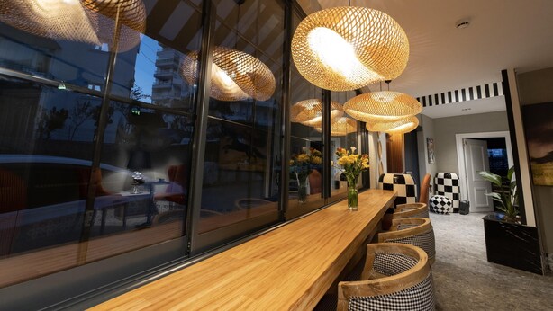A modern interior with a long wooden bench, wicker lamps, and a view through large windows. - Wolf Suites (Antalya)