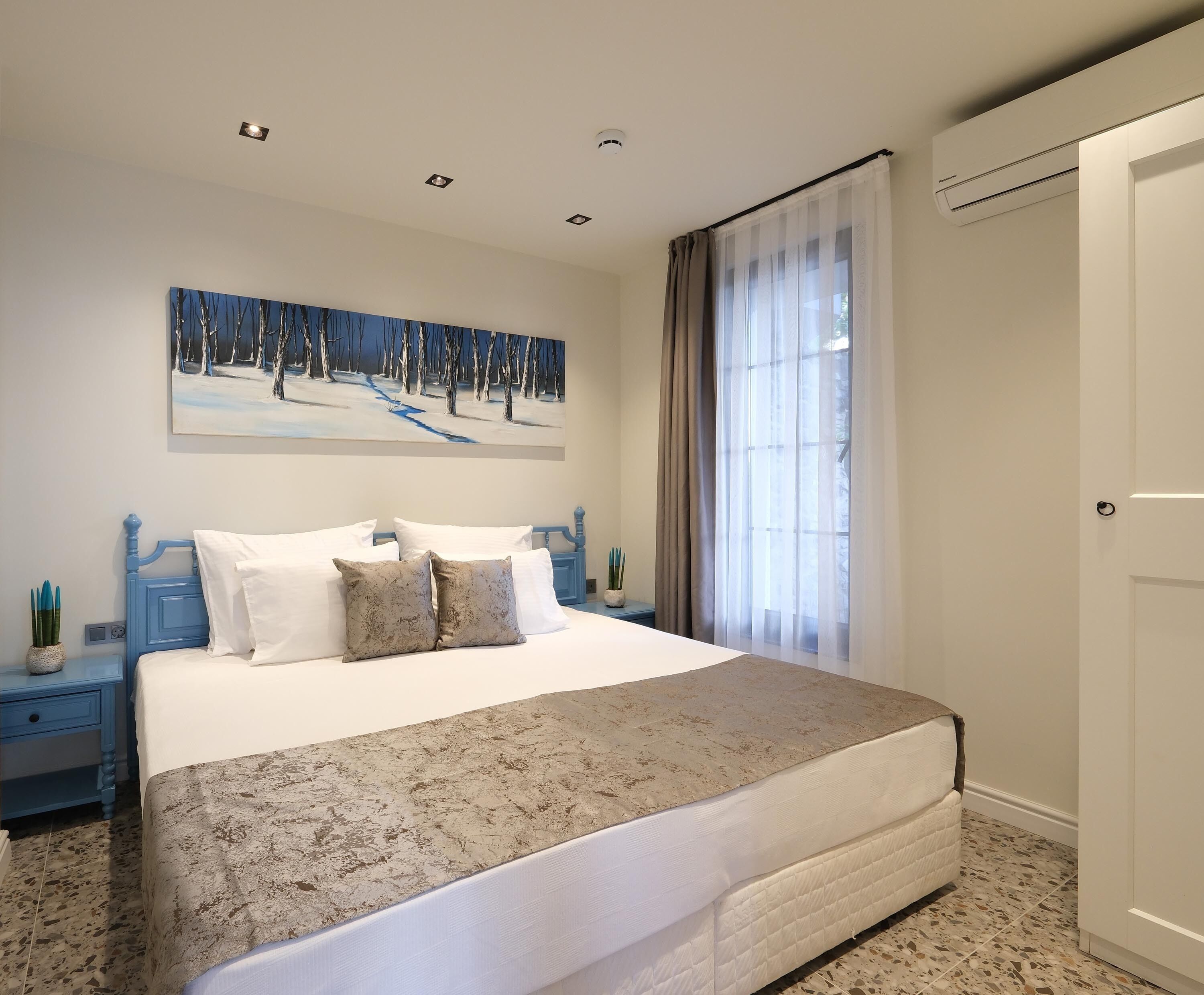 Un dormitorio con una cama grande, un cuadro de un paisaje nevado, una ventana con cortinas y una puerta.