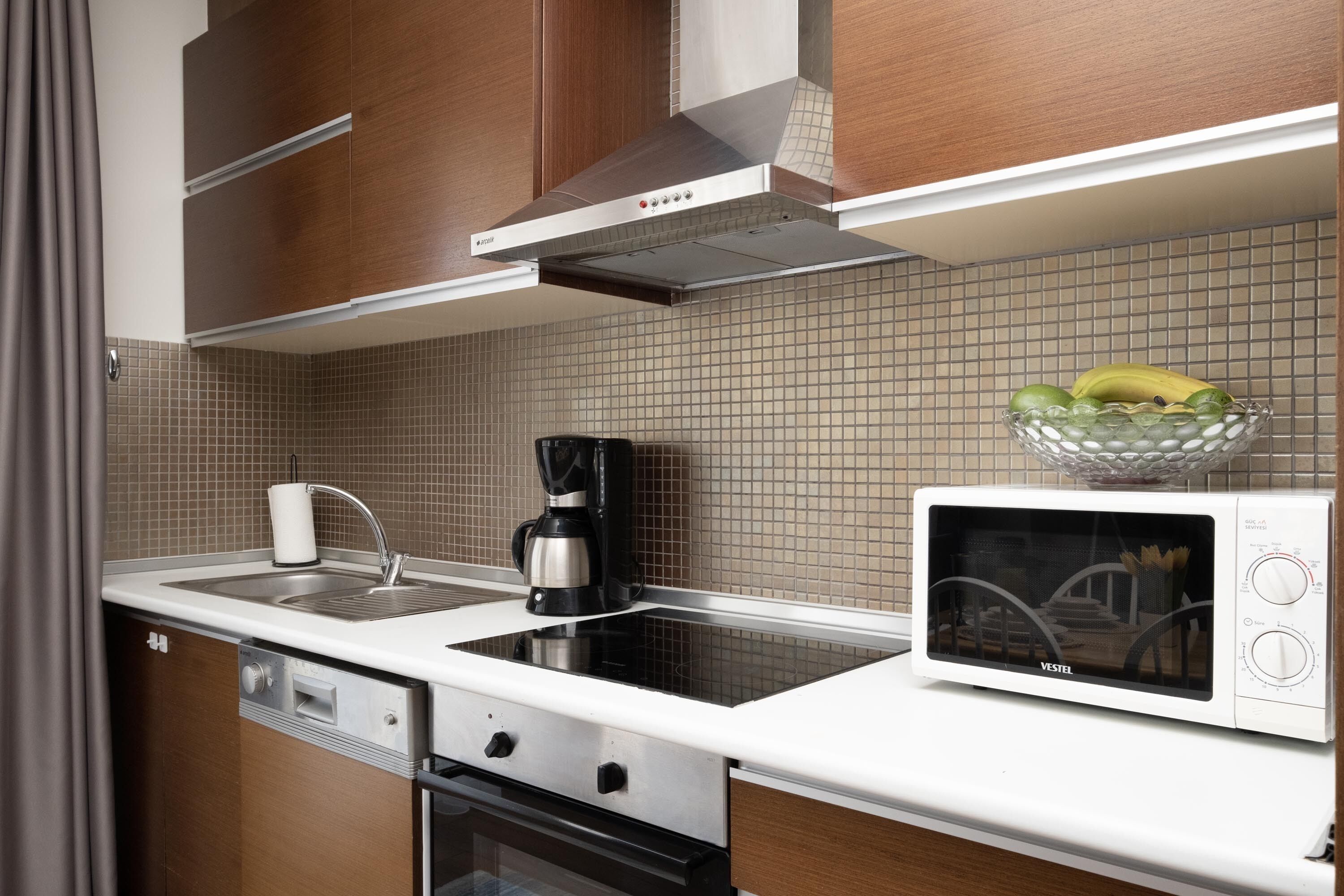 A modern kitchen with a microwave, coffee maker, and a bowl of fruit on the counter.