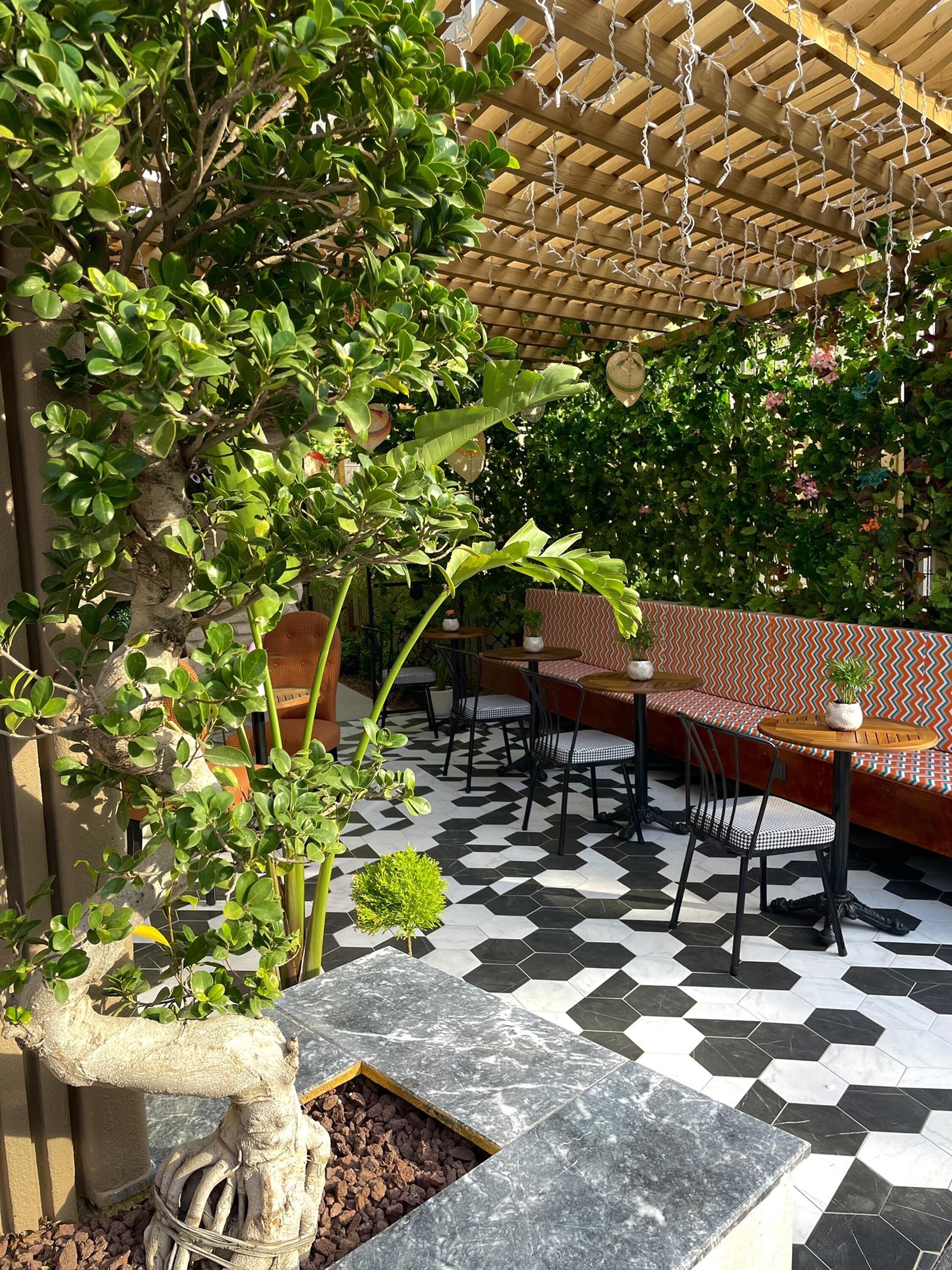 Un patio exterior con una pérgola de madera, suelo de baldosas hexagonales y arreglos de asientos.