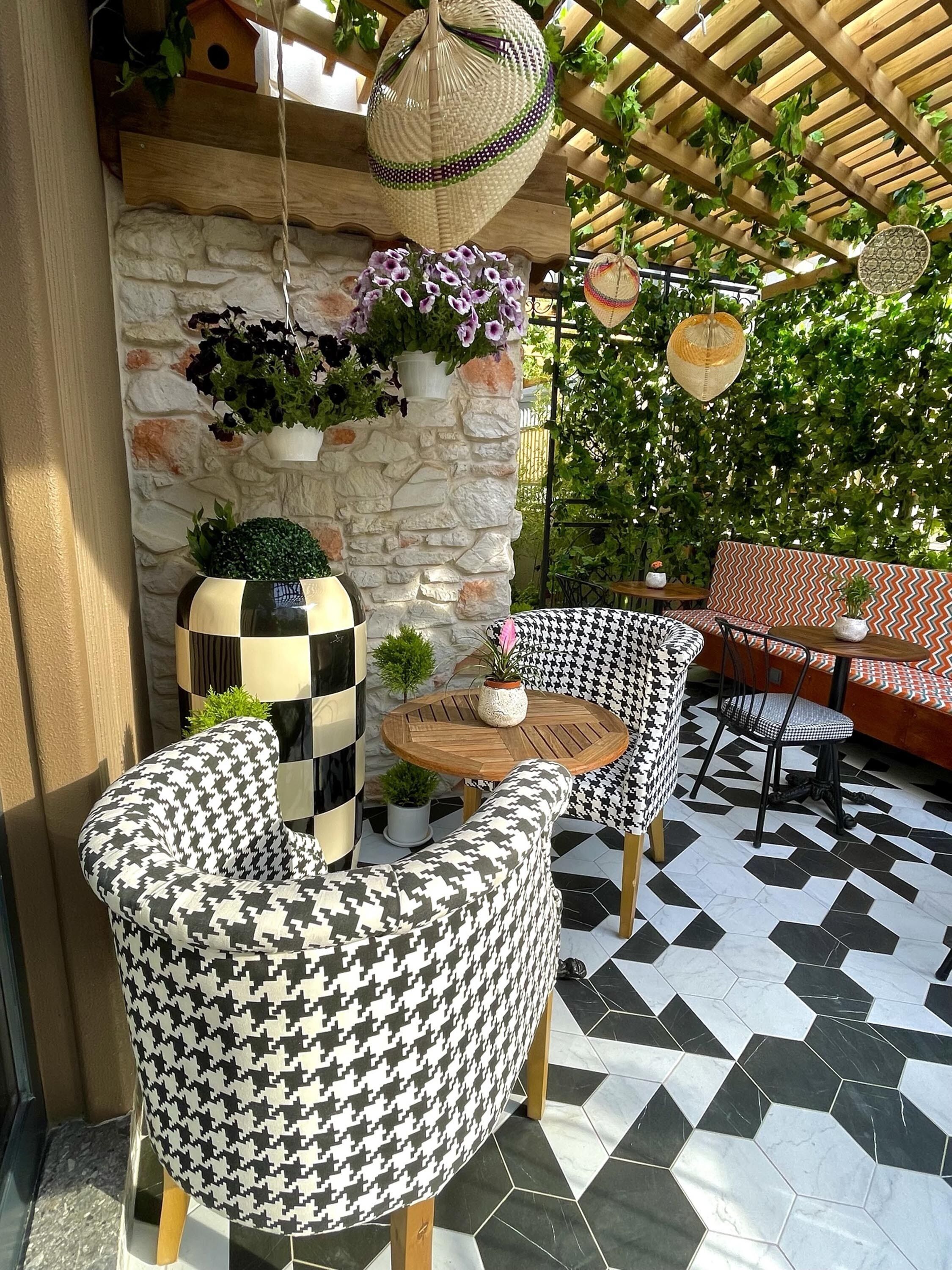 A patio area with houndstooth patterned chairs, a round wooden table, and a stone wall with hanging planters.
