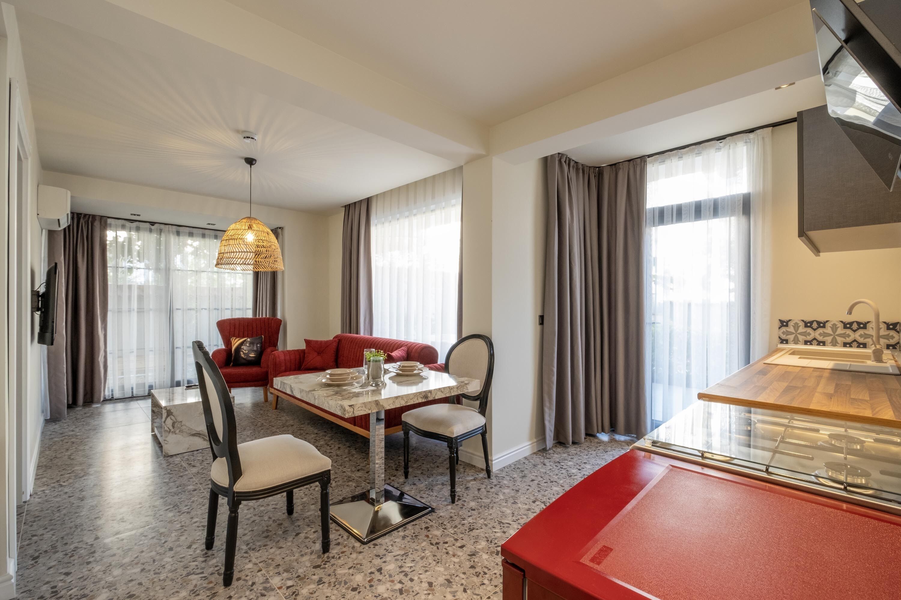 Una habitación de hotel moderna con zona de comedor, un sofá rojo y una cocina.