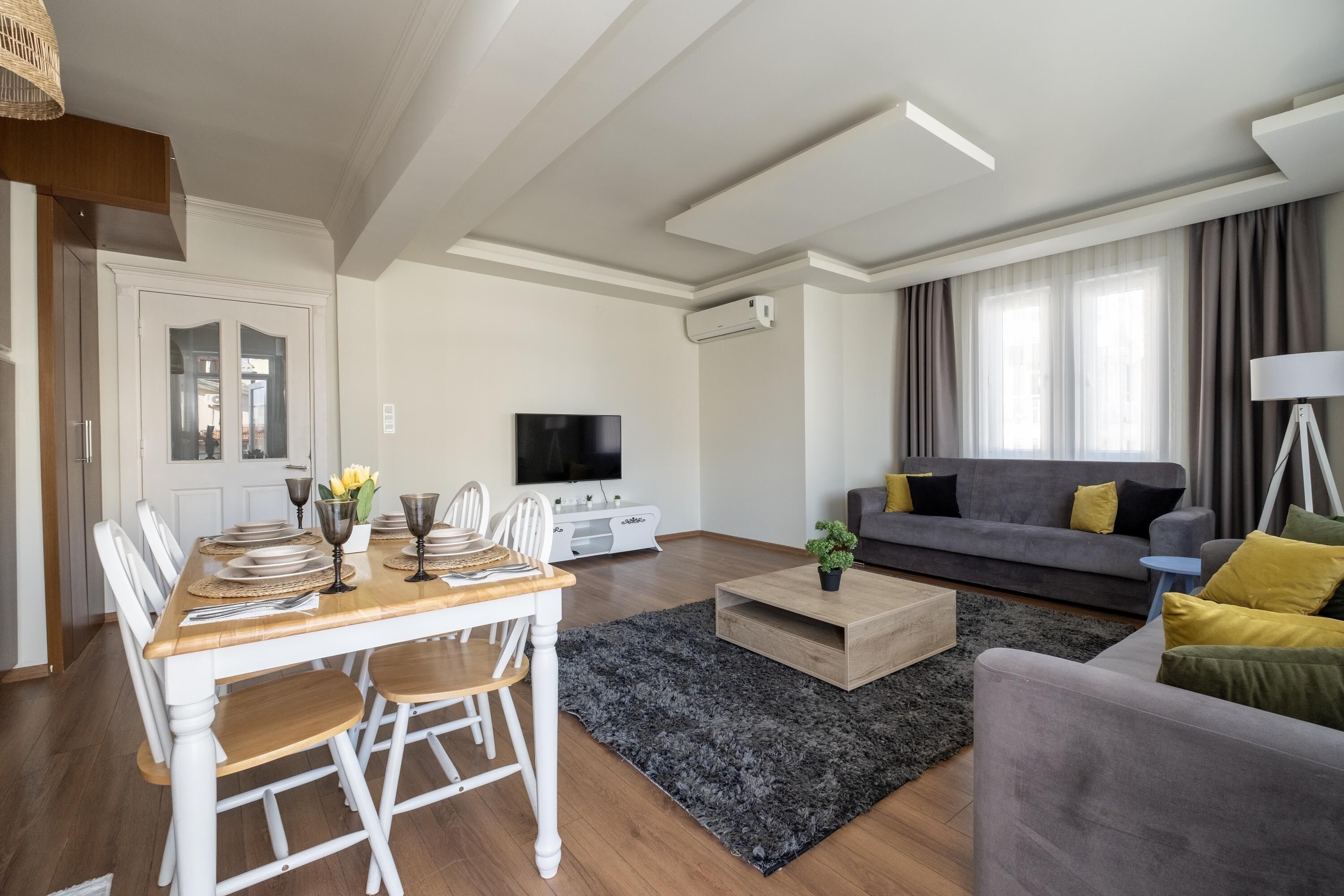 Un salon moderne avec un coin repas, un canapé gris et un téléviseur à écran plat.