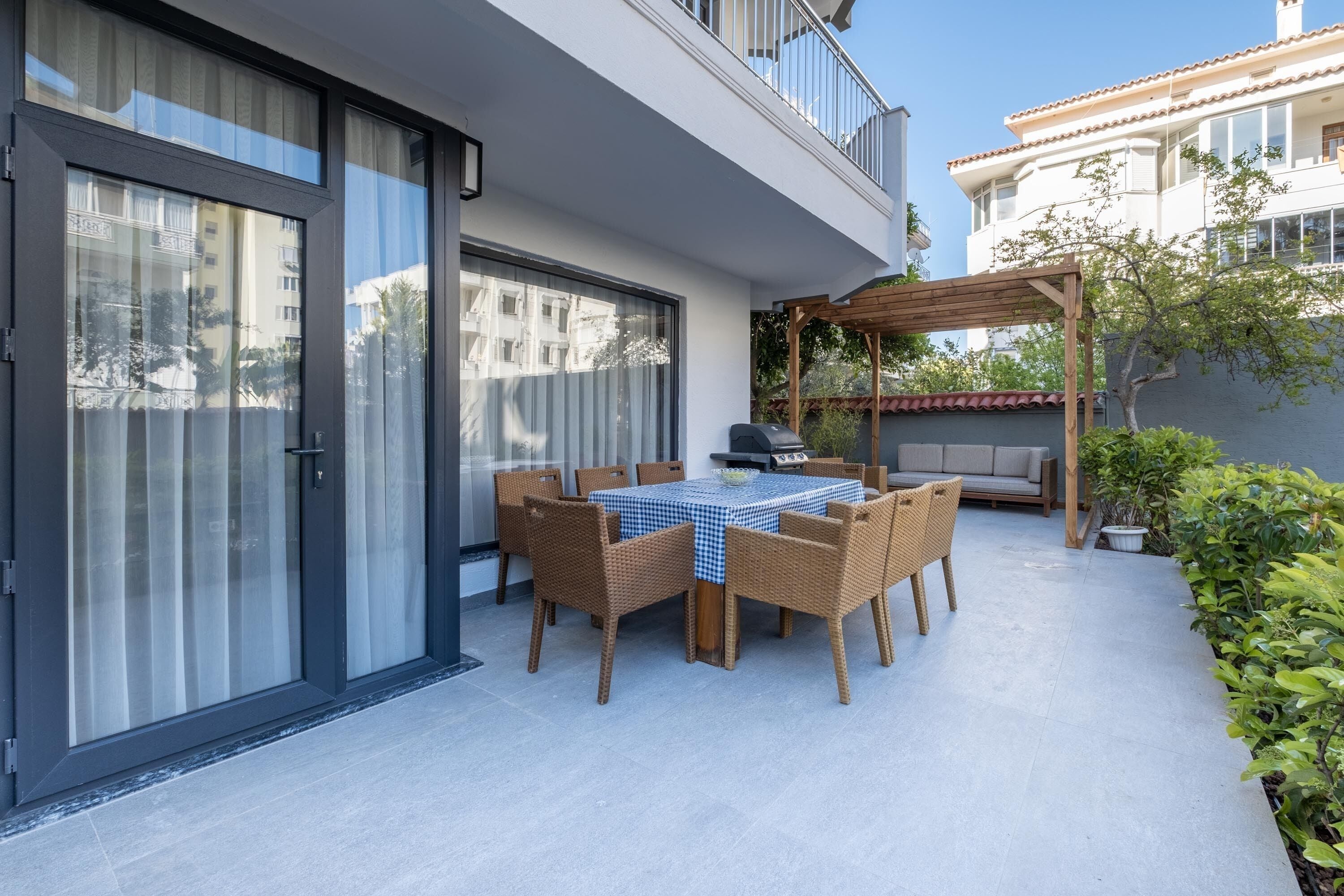 A patio with a table and chairs, a grill, and a pergola.