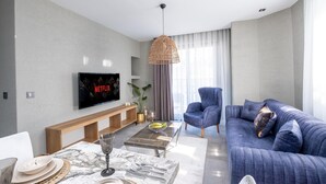 A modern living room with a sofa, a coffee table, a TV mounted on the wall, and a dining area with a bench and table. - Wolf Suites (Antalya)