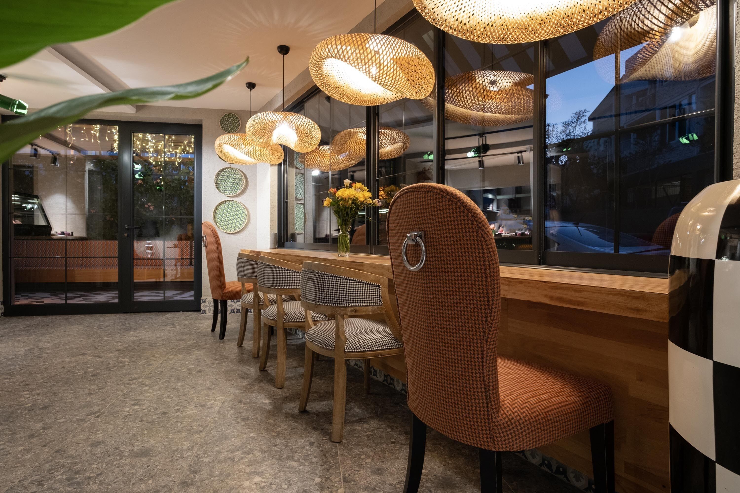 A restaurant interior with a wooden bar, checkered chairs, and woven pendant lights.