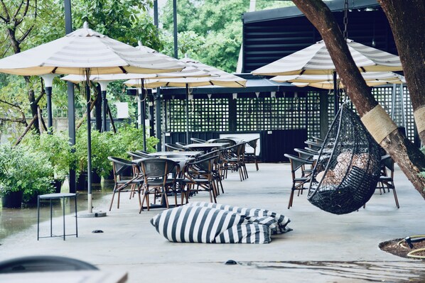 Un espacio al aire libre con mesas, sillas, sombrillas y sillones colgantes.