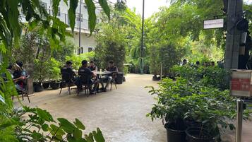 A courtyard with a group of people seated at a table, surrounded by potted plants and a sign indicating a coffee area.