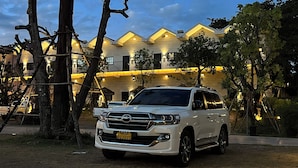 A white SUV parked in front of a building with multiple balconies and warm lighting. - Macchiato Resort Savannakhet (Savannakhet)