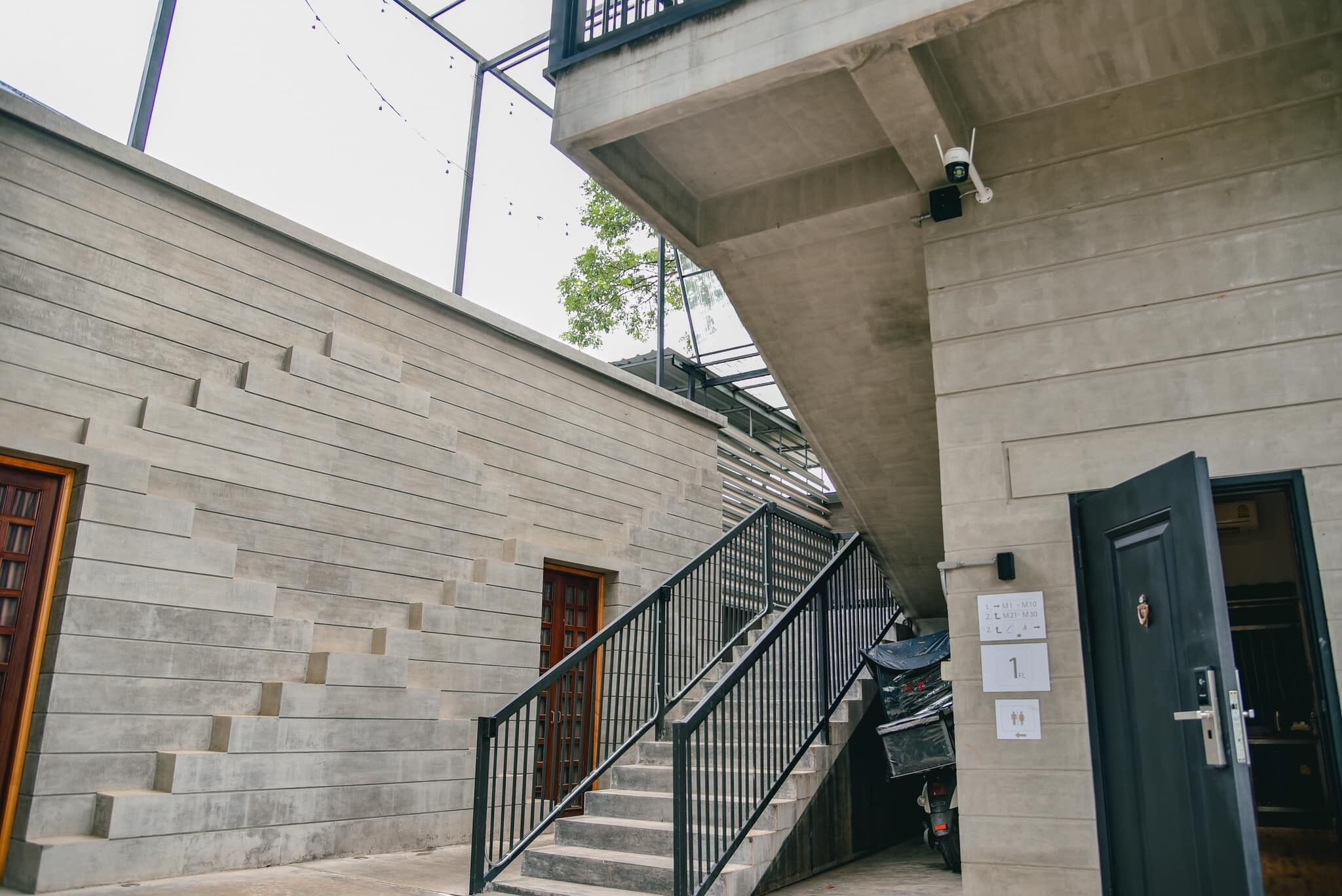 Una escalera conduce a un segundo piso con un muro de concreto y una puerta con un letrero encima.