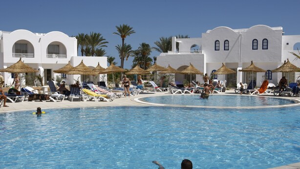 Zona de piscina con sillones de descanso y sombrillas, rodeada de edificios blancos con ventanales arqueados.