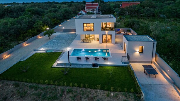 A modern two-story house with a swimming pool, outdoor seating, and a view of the mountains.