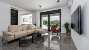 A modern living room with a beige sectional sofa, two coffee tables, a brown armchair, and a flat-screen TV mounted on the wall.