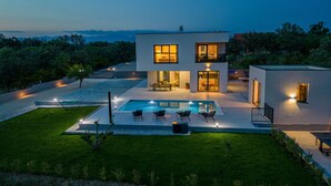 A modern two-story house with a swimming pool, outdoor seating, and a view of the sea.