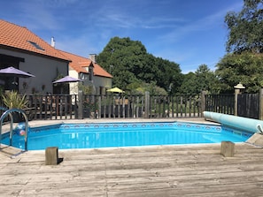 Ett trädäck som omger en rektangulär pool, och poolen har ett mönster av kakelplattor.