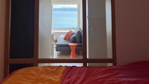 A bedroom with a large window, a bed with an orange and red blanket, and a view of the sea. - Appartment 2 rooms - Ocean View (Saint-Jean-de-Luz)