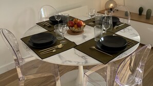 A round dining table with clear chairs, set with black plates, clear glasses, and a fruit bowl. - Appartment 2 rooms - Ocean View (Saint-Jean-de-Luz)