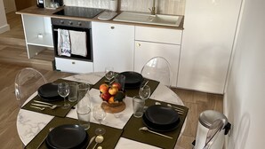 A modern kitchen with white cabinets, a built-in oven, and a sink. There is a dining table with black plates and clear glassware. - Appartment 2 rooms - Ocean View (Saint-Jean-de-Luz)