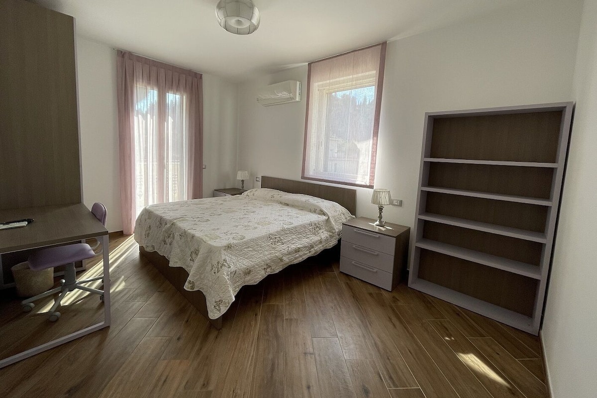 A bedroom with a bed, bedside tables, a desk, and a shelving unit.