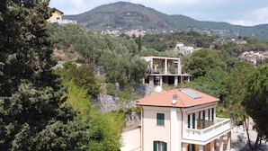 A two-story house with a balcony, surrounded by trees and hills. - Holiday Rooms La Campagnetta (Alassio)