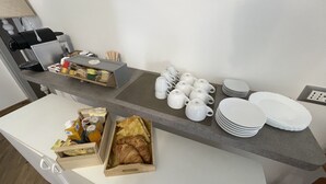 A breakfast bar with white mugs, plates, and a coffee machine. There are also croissants and juice boxes on the counter. - Holiday Rooms La Campagnetta (Alassio)