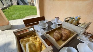A breakfast setup with bread, croissants, and juice cartons on a table with white cups and saucers. - Holiday Rooms La Campagnetta (Alassio)