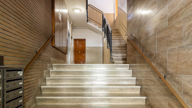 A staircase with a wooden handrail and beige steps leading to a door at the top.