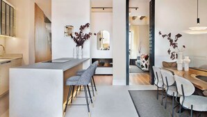 A modern kitchen with a central island, bar stools, and a dining area with a round table and chairs. - New-Beautiful Rooftop Apartment (Madrid)