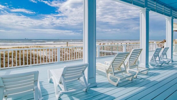 Un espace extérieur abrité, doté de chaises blanches et offrant une vue sur la plage.