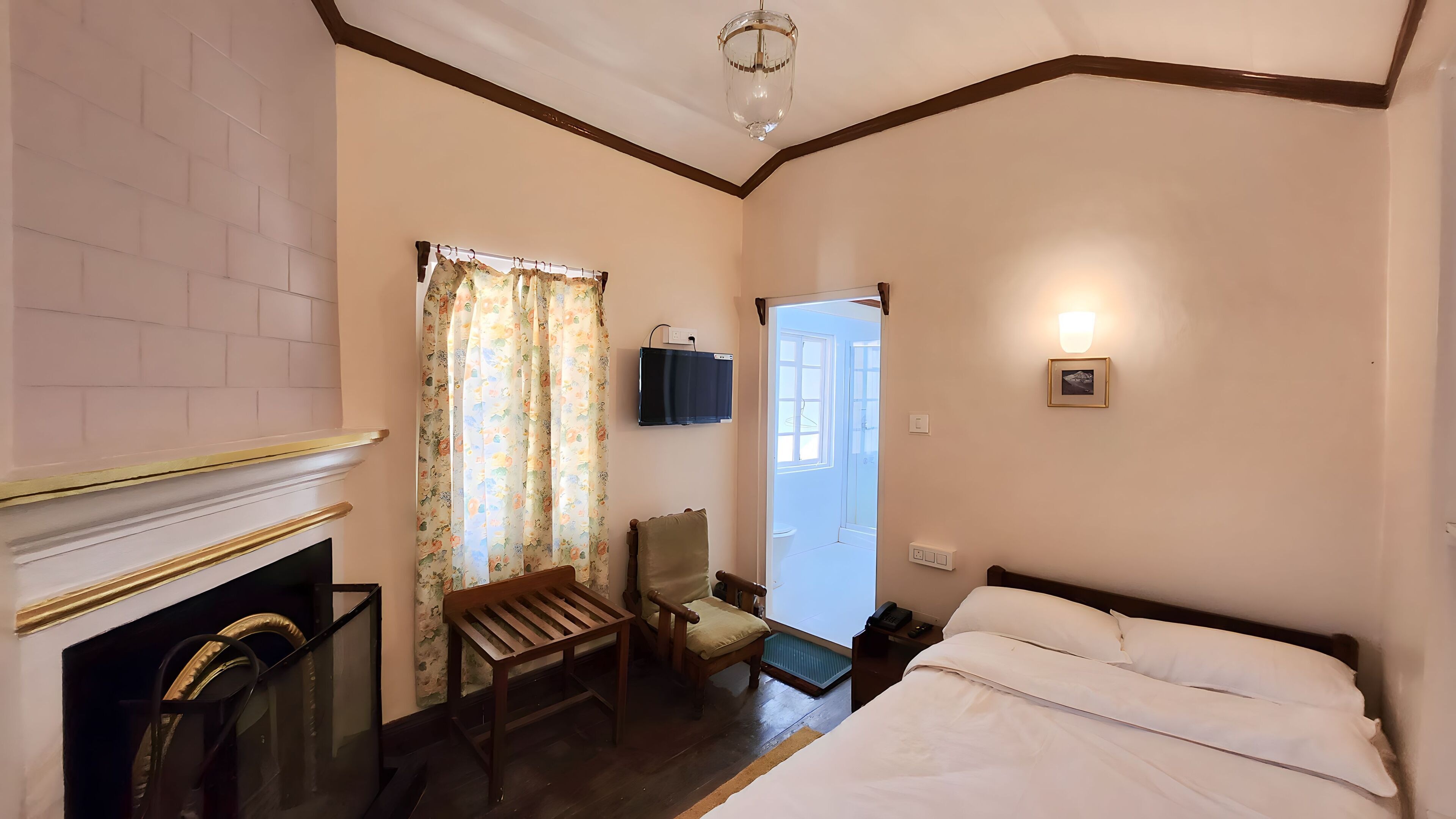 A hotel room with a bed, a chair, a fireplace, a television, and a door leading outside.