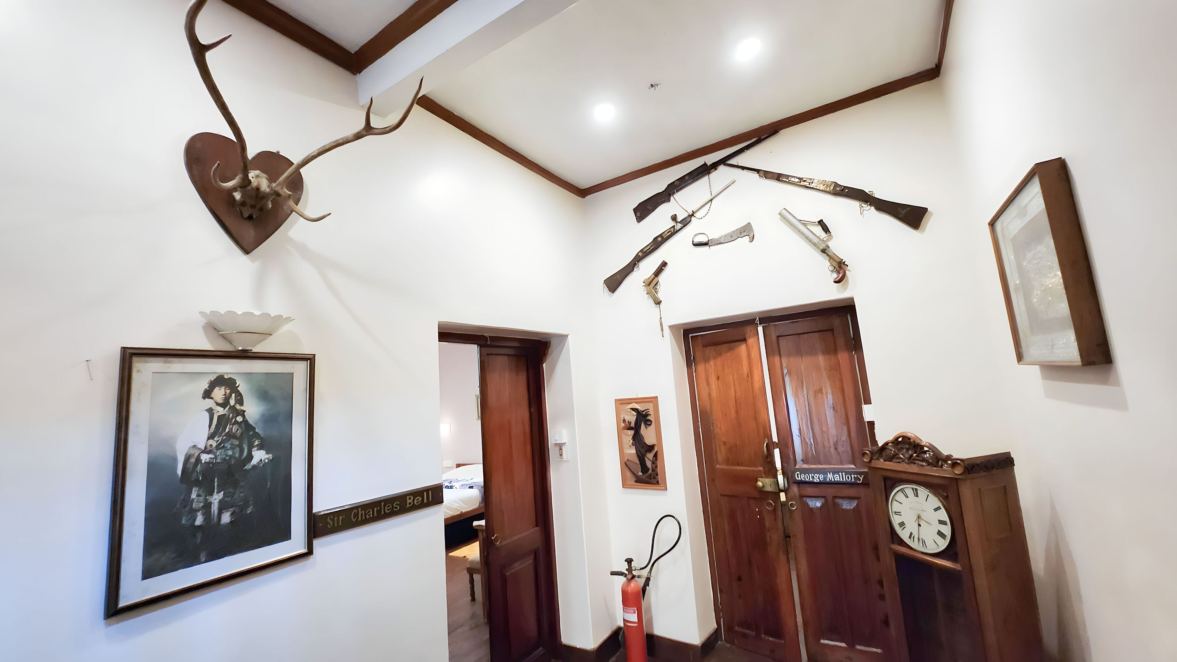 A hallway with a mounted deer head, a framed portrait, a clock, and a door labeled "George Mallory".