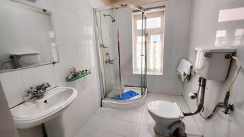 Um banheiro com chuveiro em box de vidro, pia branca, vaso sanitário e espelho.