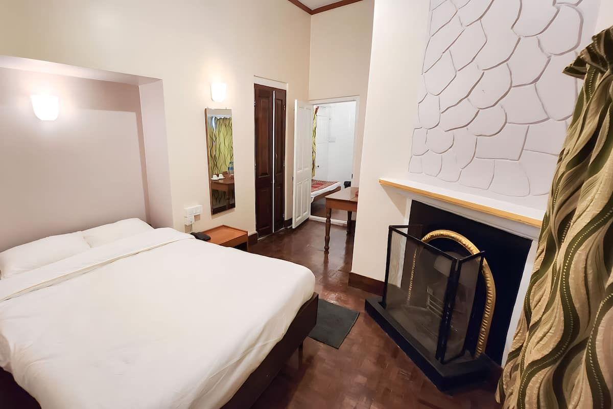 Quarto de hotel com cama, uma mesinha, espelho, lareira e guarda-roupa.