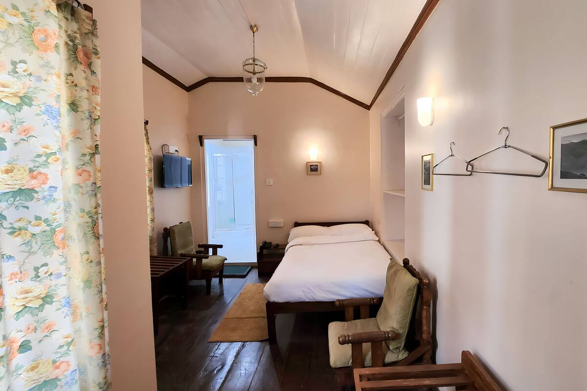 Quarto com cama, cadeira, escrivaninha, luminária de mesa, luminária pendente, moldura de quadro e porta.