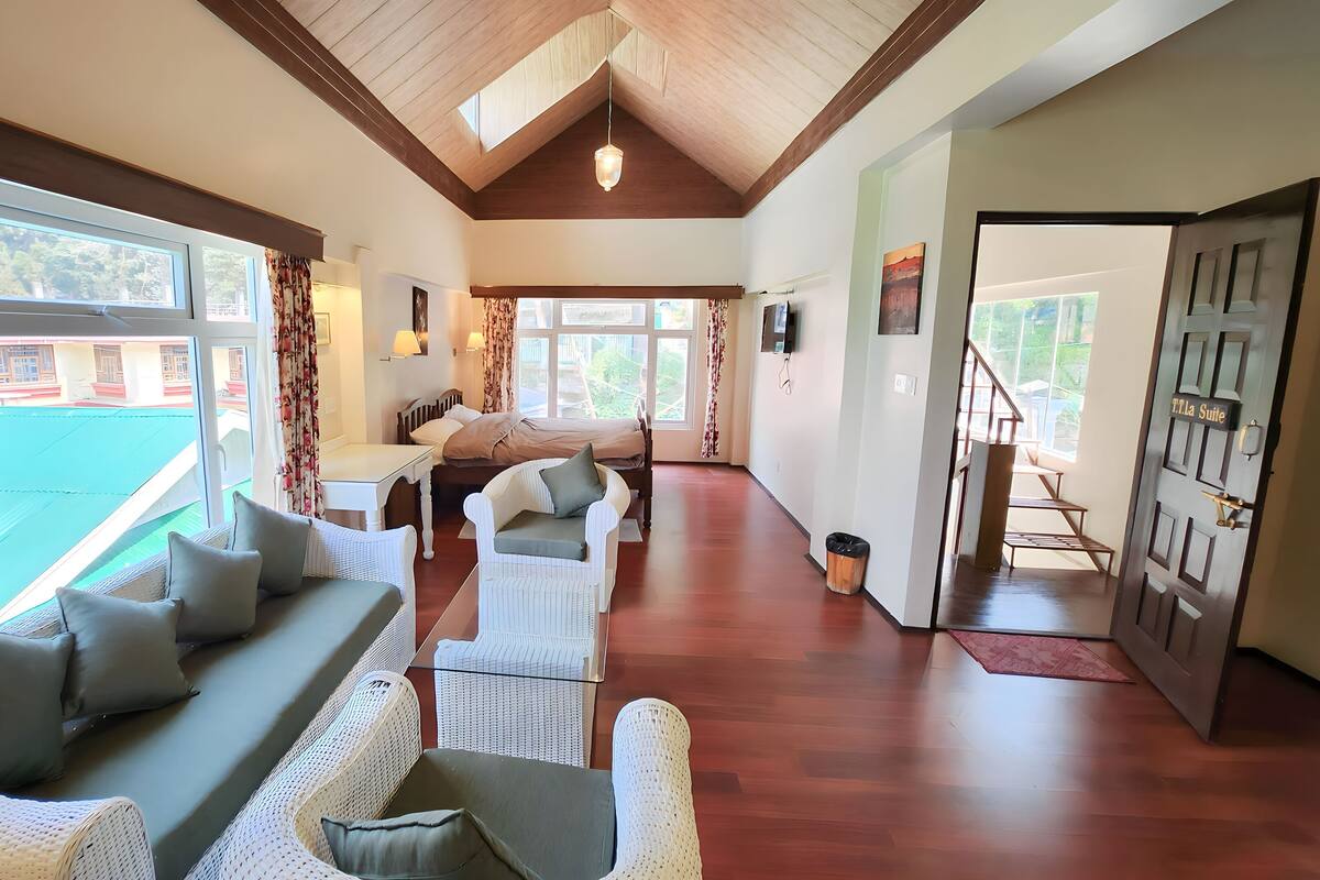 Um quarto espaçoso com teto alto, vigas de madeira, uma cama grande, um sofá e um espaço de refeições.