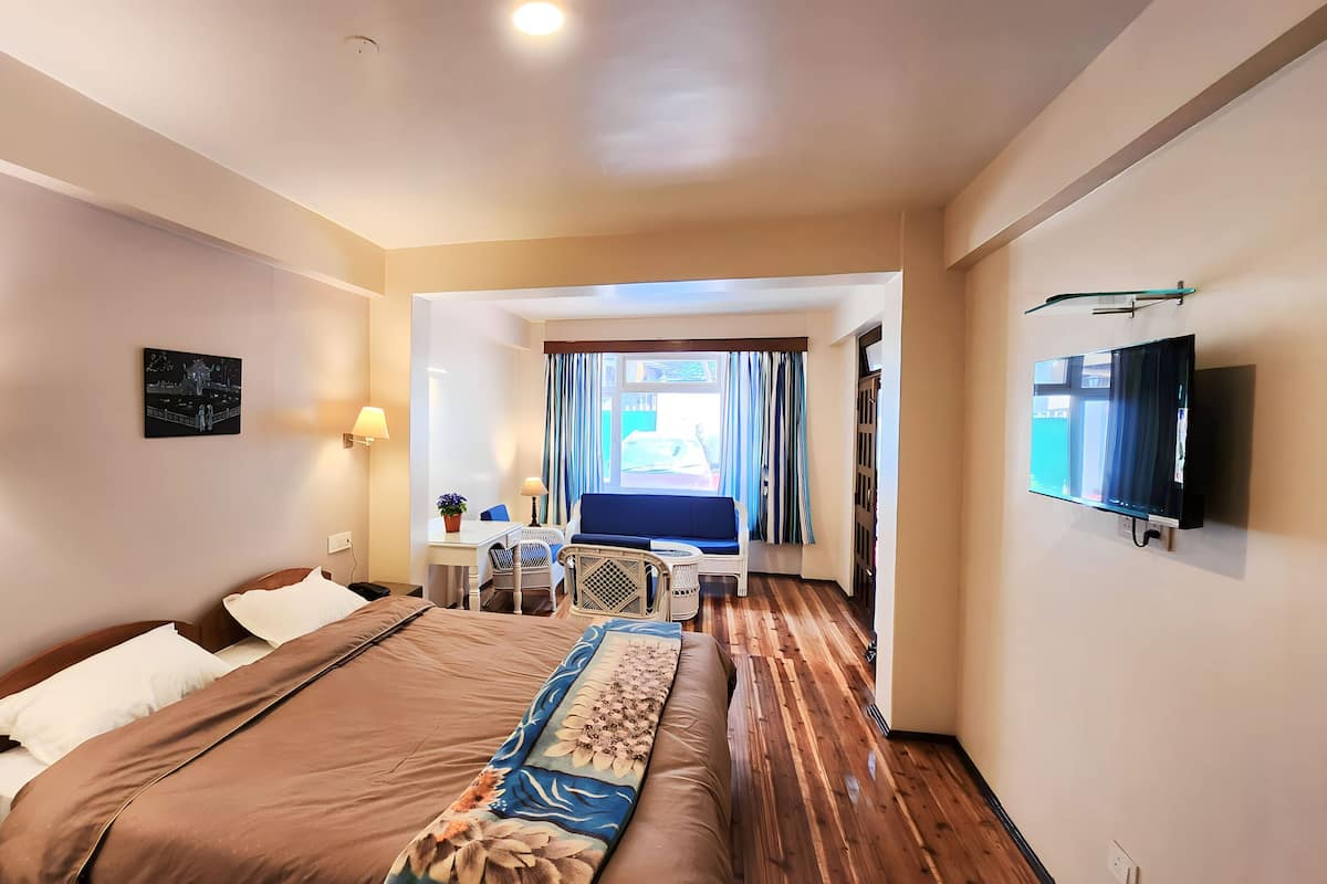 Quarto de hotel com uma cama grande, uma mesa com cadeira, televisão e janela com cortinas.