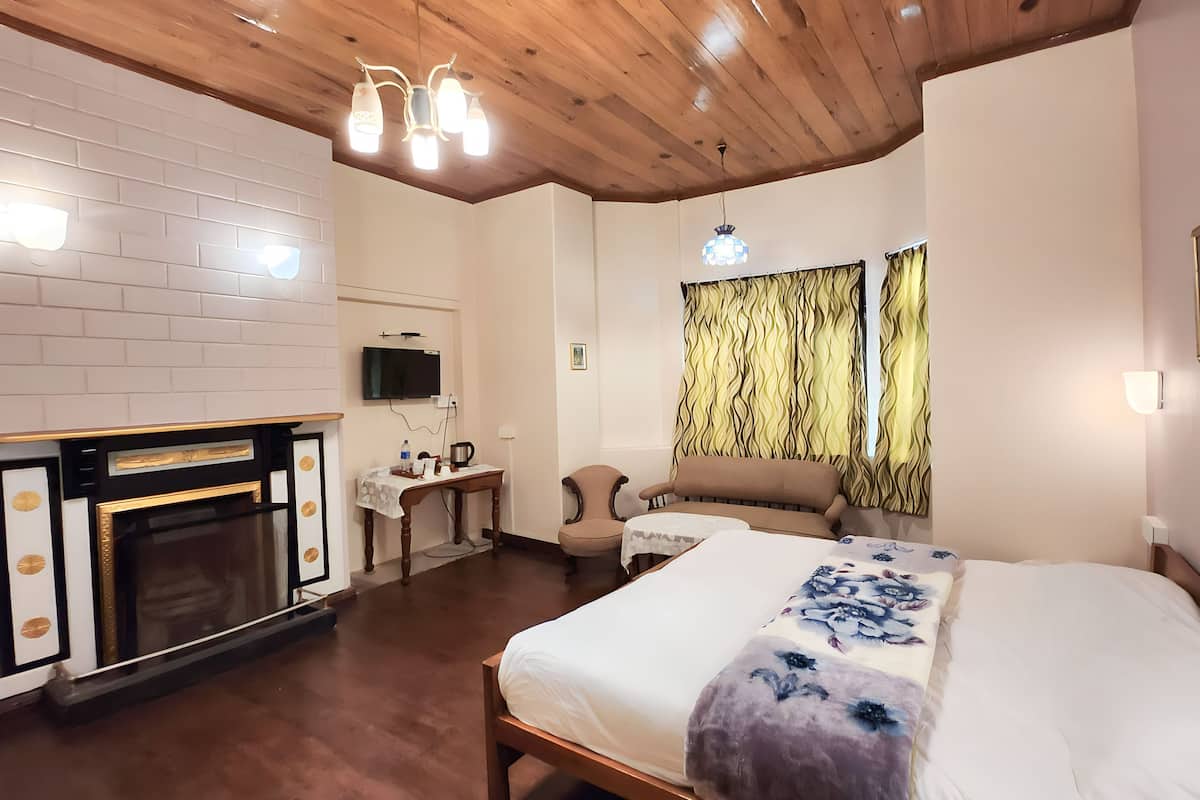 Quarto de hotel com lareira, cama com roupa de cama floral, teto de madeira e televisão na parede.