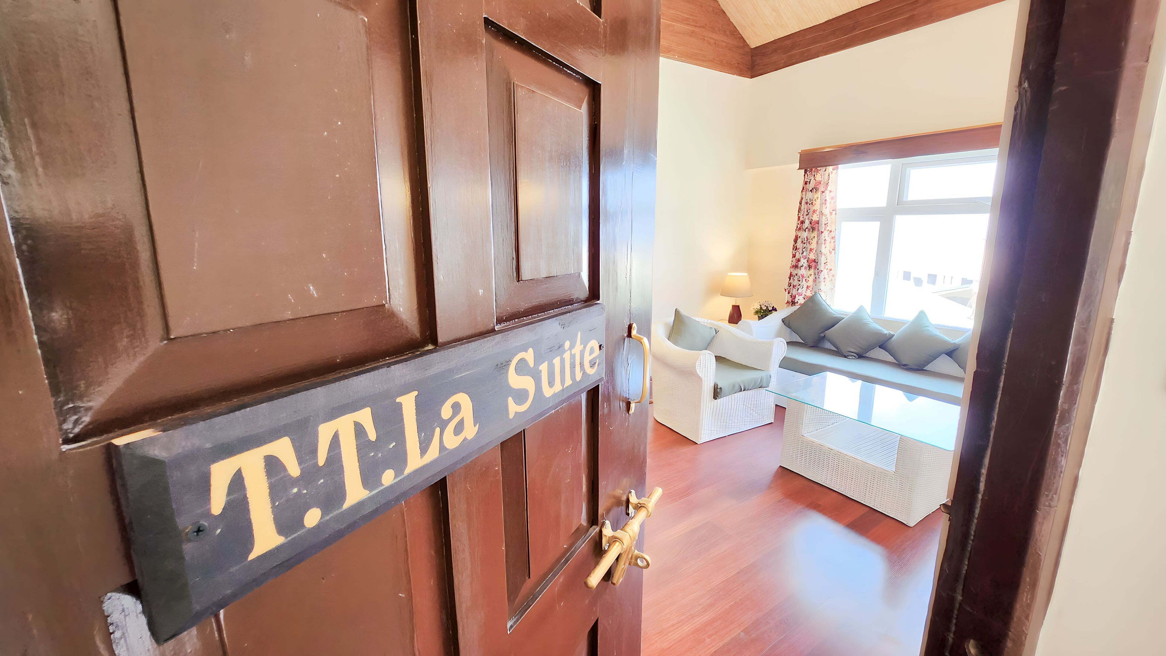 A wooden door with a sign reading "T.T.La Suite" and a glimpse of a living room with a sofa and a window.
