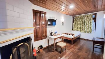 Una habitación con techo de madera, una cama, un escritorio con silla, chimenea y televisión.