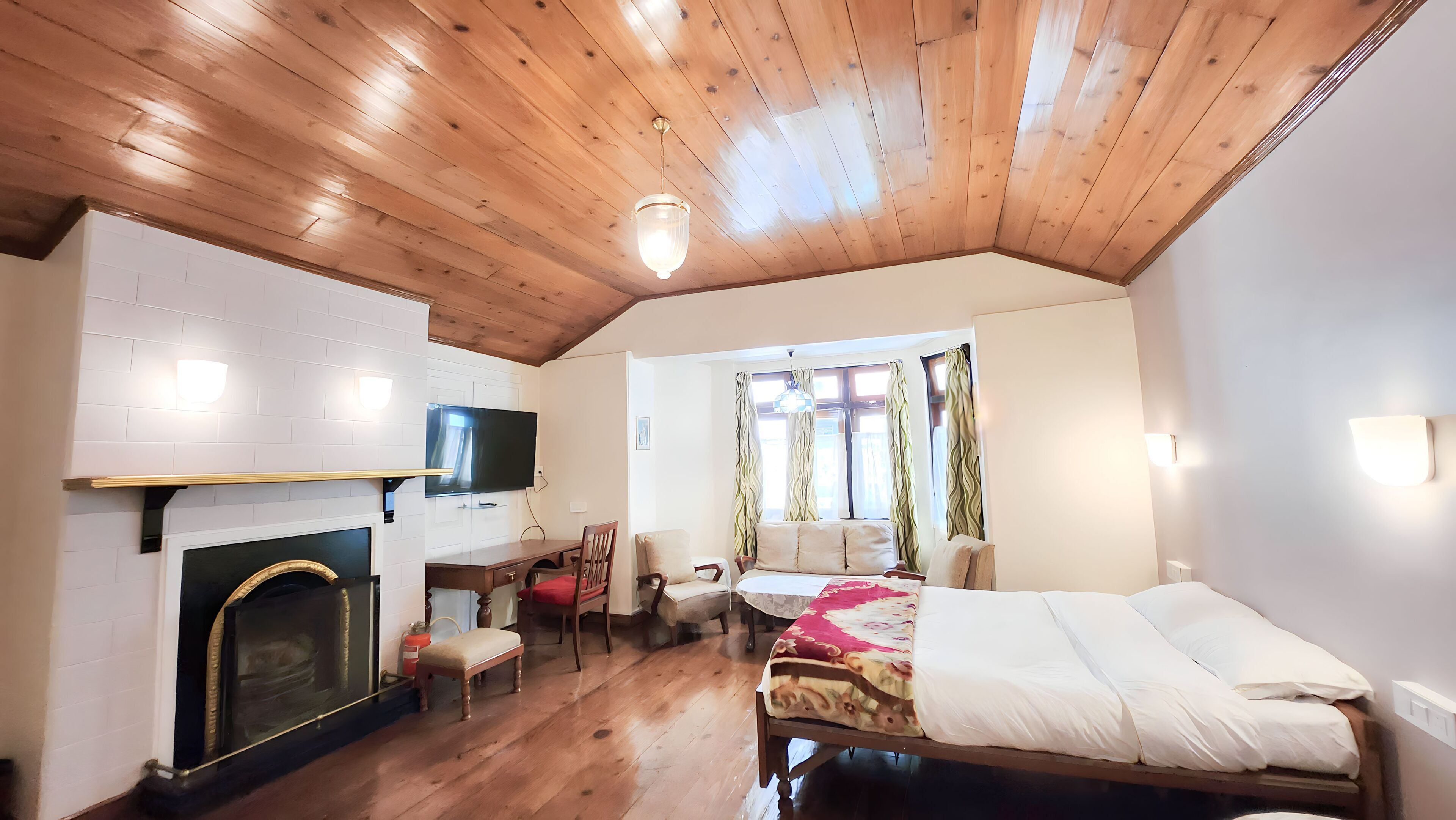A cozy room with a wooden ceiling, a fireplace, a bed, a TV, and a window with curtains.